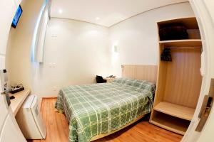 a small room with a bed with a green plaid blanket at Golden Hotel - O MAIS CENTRAL - Pet Friendly in Chapecó