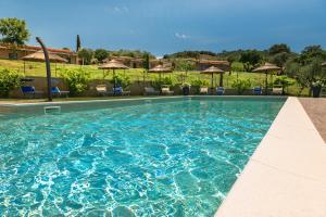 a swimming pool with blue water and chairs and umbrellas at Podere n°8 Agriturismo in Maremma in Alberese