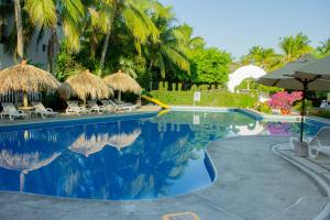 a swimming pool with chairs and umbrellas next to a resort at Hotel Castillo Huatulco & Beach Club in Santa Cruz Huatulco