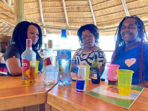 tres mujeres sentadas en una mesa con botellas de alcohol en Mabata Makali Luxury Tented Camp, en Ruaha National Park
