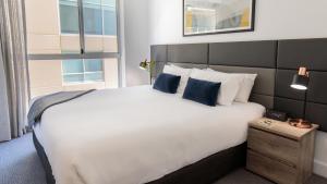 a bedroom with a large white bed with blue pillows at Oaks Glenelg Plaza Pier Suites in Adelaide