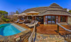 uma casa com telhado de palha e uma piscina em Motswiri Private Safari Lodge em Madikwe Game Reserve
