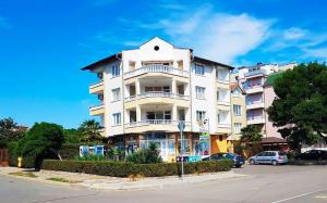 ein großes weißes Apartmenthaus mit Autos auf einem Parkplatz in der Unterkunft Kirovi House - guest rooms in Zarewo