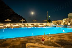 a large blue swimming pool at night with a drink at Marianna Hotel in Perissa