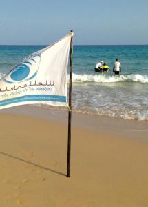 a sign on the beach with people in the ocean at Wellenkind Surfschool in La Pared