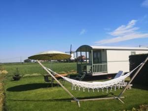 a hammock and an umbrella in front of a trailer at Roulotte Hartemeers in Tielt