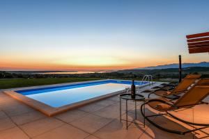 a swimming pool on a patio with chairs and a sunset at Vila Matak in Ražanac