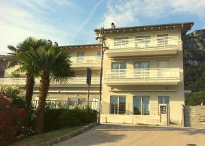um edifício branco com uma palmeira em frente em Amarillys Apartment and Rooms in CasaClima (climate certification) em Nago-Torbole