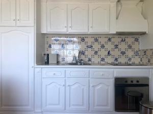 una cocina con armarios blancos y azulejos azules y blancos en La VIGIE de CASTELROCK ( Casa Petunia ), en Mosteiros