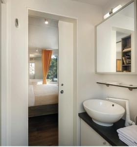 baño con lavabo y cama con espejo en Victoria Mobilehome in Padova Premium Camping Resort en Banjol