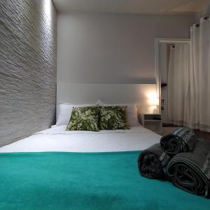 um quarto com uma cama branca com lençóis e almofadas verdes em Loft encantador B - 8 km de Floripa em São José