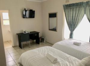 a bedroom with two beds and a desk and a television at White House lodge in Mthatha