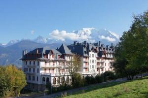 un grand bâtiment sur une colline avec une montagne en arrière-plan dans l'établissement Résidence du Mont-Blanc n°5Bis, à Combloux 5 autres photos