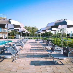 una fila di sedie a sdraio con ombrelloni accanto alla piscina di Sabbia & Mare a Rosolina Mare