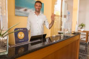 a man standing behind a counter with his hand up at Hotel Greta B&B in Rimini