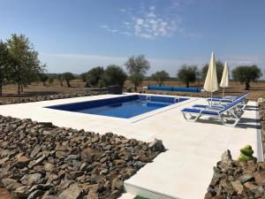 a swimming pool with a rock wall and two chairs and umbrellas at Horta da Rosa - Adults Only in Alvito