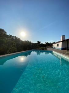 een groot blauw zwembad met de zon op de achtergrond bij Monte das Pedras - Avis in Avis