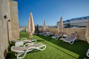 una fila di sedie a sdraio e ombrelloni sul tetto di Allegro Hotel a San Giuliano