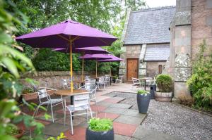 un patio con mesas y sillas con sombrillas púrpuras en The Auld Kirk, en Ballater