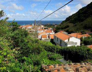 um grupo de casas numa colina com o oceano em O Palheiro em Faja Grande