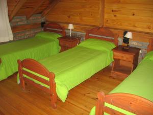 um quarto com 2 camas verdes e pisos em madeira em Cabañas Lorien em Esquel