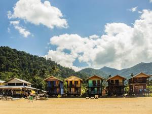 a row of houses on a beach with mountains in the background at Beach Shack Chalet - Garden View Aframe Big Unit in Tioman Island