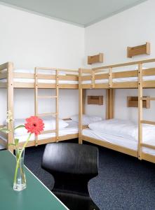 a room with three bunk beds with a table and a vase with a flower at Jugendgästehaus des CVJM Berlin-Kaulsdorf in Berlin