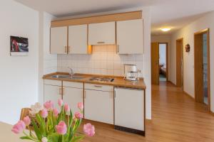 a kitchen with white cabinets and a vase of pink flowers at Rustikale 3 Zi.-FeWo Nähe Freiburg 70qm in Simonswald