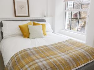 Cama blanca con almohadas amarillas y ventana en Pine Cottage en Sedbergh
