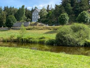 une rivière dans un champ avec une maison en arrière-plan dans l'établissement La Margeride, à Serverette