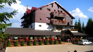 a large wooden building with flowers in a parking lot at Pensiunea Skiland in Muntele Băişorii