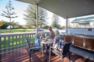 una mujer y dos niños sentados en una mesa en una cubierta en Werri Beach Holiday Park, en Gerringong