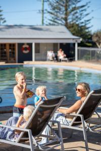 a woman and two children sitting in lawn chairs by a pool at Werri Beach Holiday Park in Gerringong