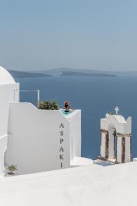 a person sitting on top of a white building next to the water at Aspaki by Art Maisons in Oia