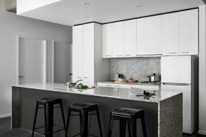 a kitchen with white cabinets and a counter with stools at Punthill Apartment Hotel - Manhattan in Melbourne