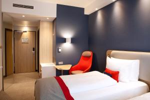 ラウンハイムにあるHoliday Inn Express Frankfurt Airport - Raunheim, an IHG Hotelのベッドと赤い椅子が備わるホテルルームです。