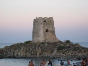 people standing on the beach in front of a tower in the water at Il Mirto in Bari Sardo