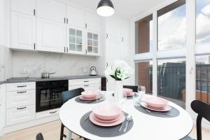 a white kitchen with a table with pink dishes on it at Apartamenty Rajska 8 - Gdańsk Stare Miasto by Renters in Gdańsk