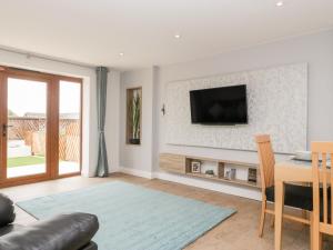 a living room with a table and a television on a wall at Honey Bee Retreat in Axminster