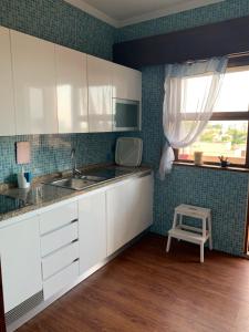 uma cozinha com armários brancos, um lavatório e uma janela em A Casa das Margaridas no Porto