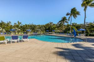 una piscina con sillas, sombrillas y palmeras en Ocean Point #2210, en Tavernier