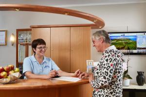 two women are standing at a counter talking at Akzent Hotel Atrium Baden in Bad Krozingen