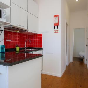 una cocina con armarios blancos y una pared de baldosas rojas en Apartamentos com Historia, en Coímbra