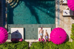 Ein Mann und zwei Frauen sitzen neben einem Pool mit rosa Sonnenschirmen in der Unterkunft PinkPrivate Sanur - for Cool Adults Only in Sanur