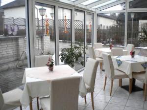 un restaurante con mesas blancas, sillas blancas y ventanas en Gockescher Hahn, en Pöhl