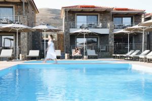 a woman in a white dress walking by a swimming pool at Costa D' Ifesto in Agios Ioannis Kaspaka