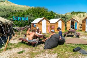 um grupo de pessoas sentadas numa mesa de piquenique em frente a uma cabana em Surfana Beach camping hostel Bed & Breakfast Vlieland em Vlieland