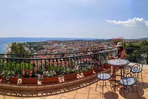 a woman sitting at a table on a balcony with plants at VelaLatina Residence B&B Soverato in Soverato Marina