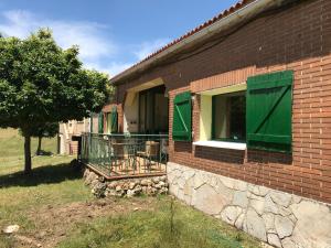 een stenen huis met groene ramen en een boom bij La Masía de Navas in Navas del Pinar