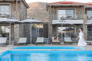 a woman in a white dress walking by a swimming pool at Costa D' Ifesto in Agios Ioannis Kaspaka